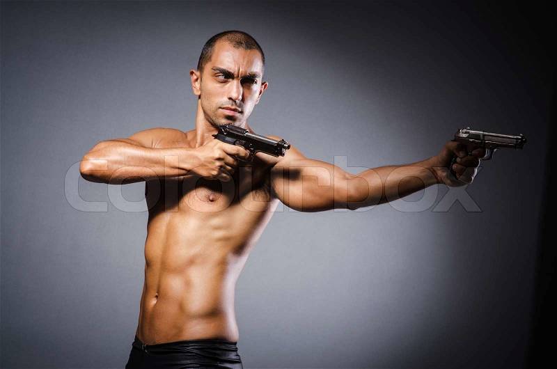 Ripped man with gun against grey background, stock photo