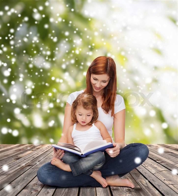 Childhood, parenting, people and education concept - happy mother with little girl reading book over wooden floor and green plants background, stock photo