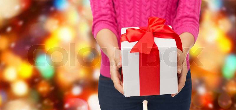 Christmas, holidays and people concept - close up of woman in pink sweater holding gift box over red lights background, stock photo