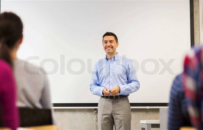 Education, high school, teamwork and people concept - smiling teacher standing in front of white board and students in classroom, stock photo