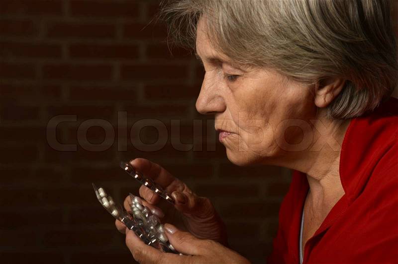 Older sick woman in red with pills on a background of a brick, stock photo