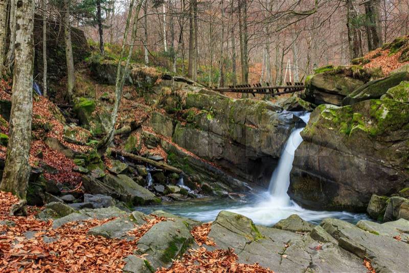 Incredibly beautiful and clean little waterfall with several cascades over large stones in the forest comes out of a huge rock covered with moss, stock photo