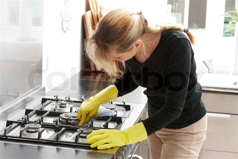 A caucasian woman cleaning the gas stove, stock photo