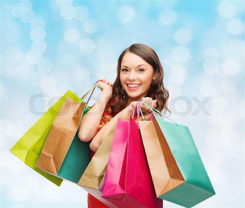 Sale, gifts, christmas, holidays and people concept - smiling woman with colorful shopping bags over blue lights background, stock photo