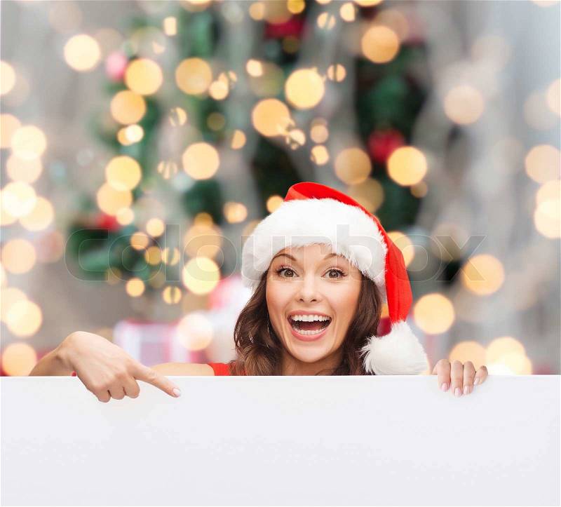 Christmas, x-mas, people, advertisement and sale concept - happy woman in santa helper hat with blank white board over tree lights background, stock photo