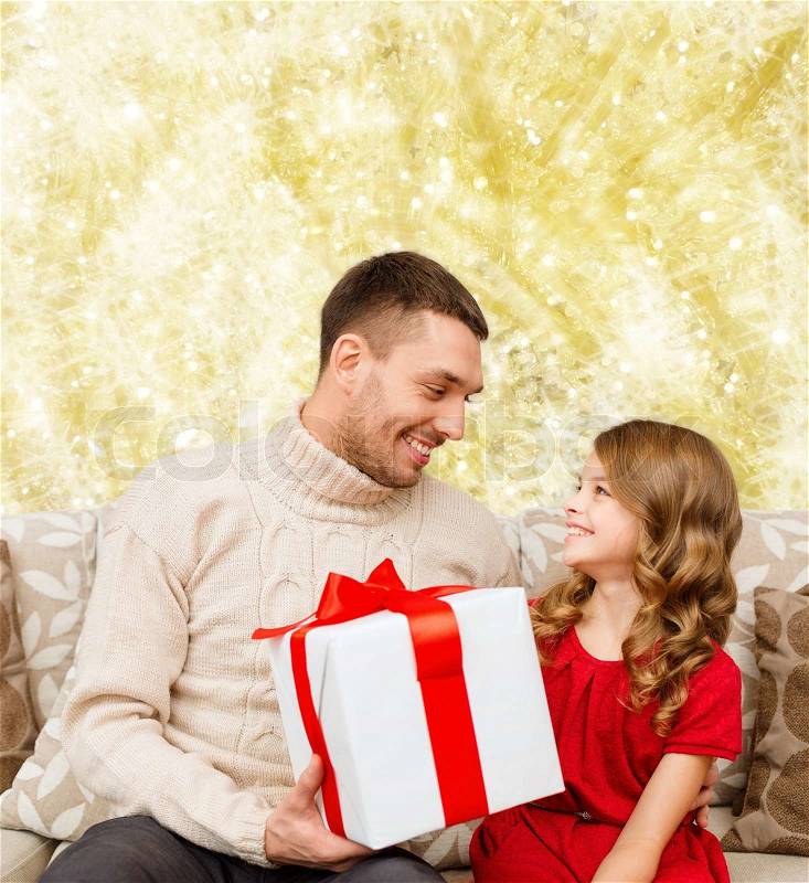 Family, christmas, holidays and people concept -smiling father and daughter with gift box over yellow lights background, stock photo