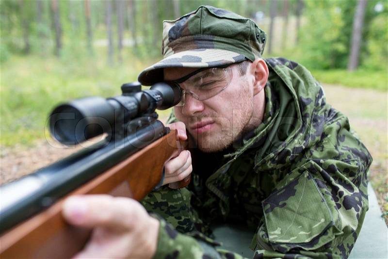 Hunting, war, army and people concept - close up of young soldier, ranger or hunter with gun in forest, stock photo