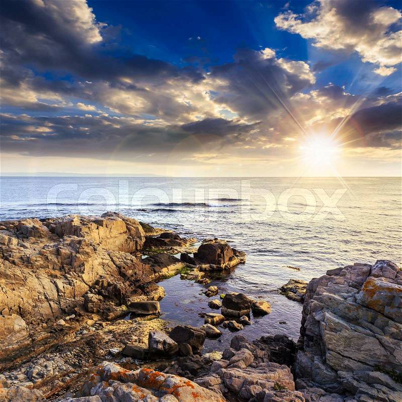 Calm sea with fiev waves on coast with boulders and seaweed at sunset, stock photo