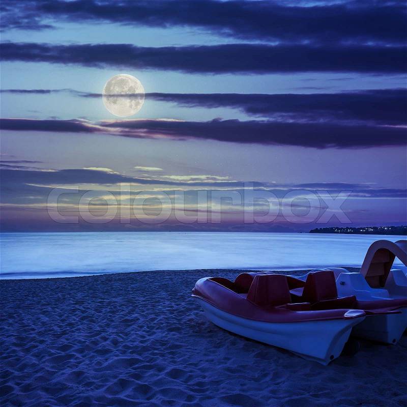 Calm sea waves touch sandy beach with few boats at night in moon light, stock photo