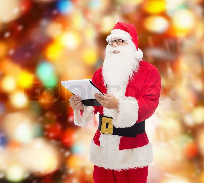 Christmas, holidays and people concept - man in costume of santa claus with notepad over red lights background, stock photo