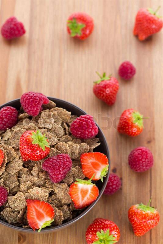 Bran flakes with fresh raspberries and strawberries on wooden table. Healthy eating choice concept, stock photo