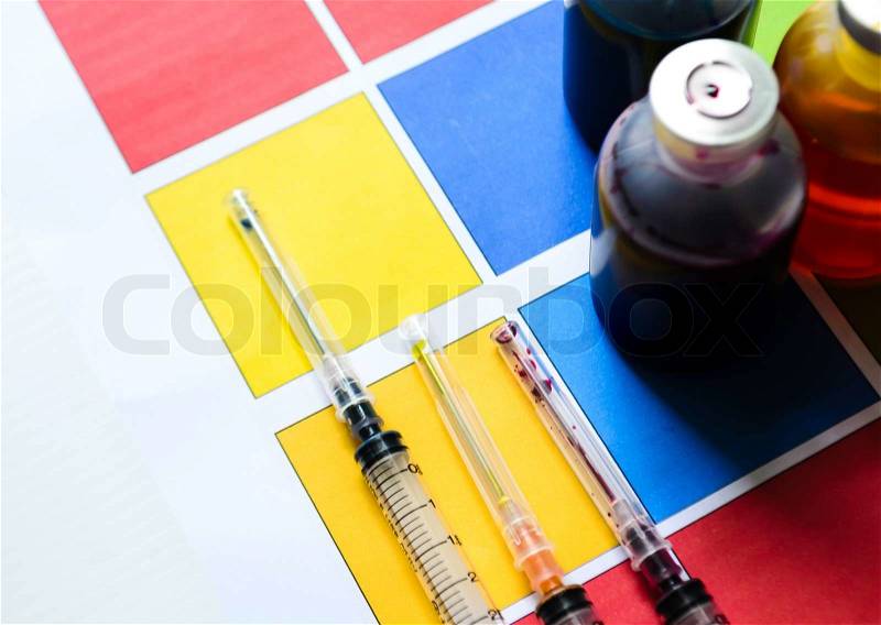 Bottle of ink printer has three colors. Colors is red, yellow and blue with syringe on colored paper, stock photo