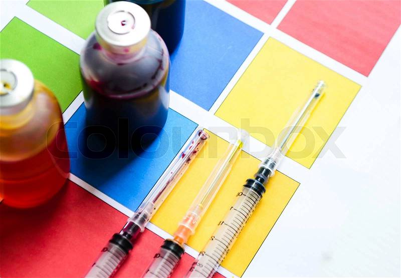 Bottle of ink printer has three colors. Colors is red, yellow and blue with syringe on colored paper, stock photo