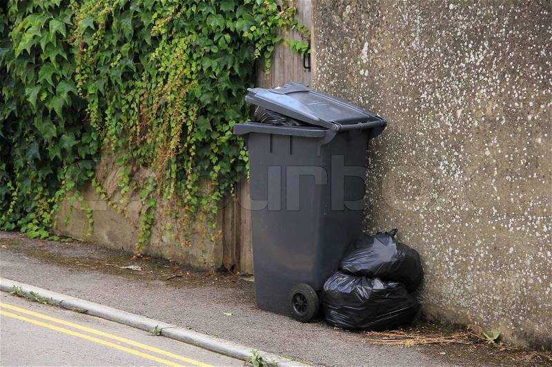 The grey garbage can and black bags wait for the weekly pick-up service in England, stock photo