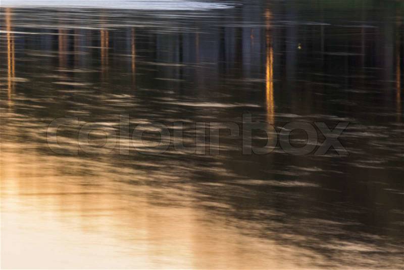 City river abstract background. reflection of city lights in the rippled water of the river surface on ling exposure at sunset, stock photo