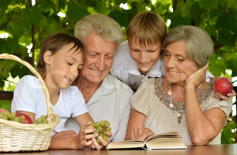 Grandparents with her grandson reading in summer at table, stock photo
