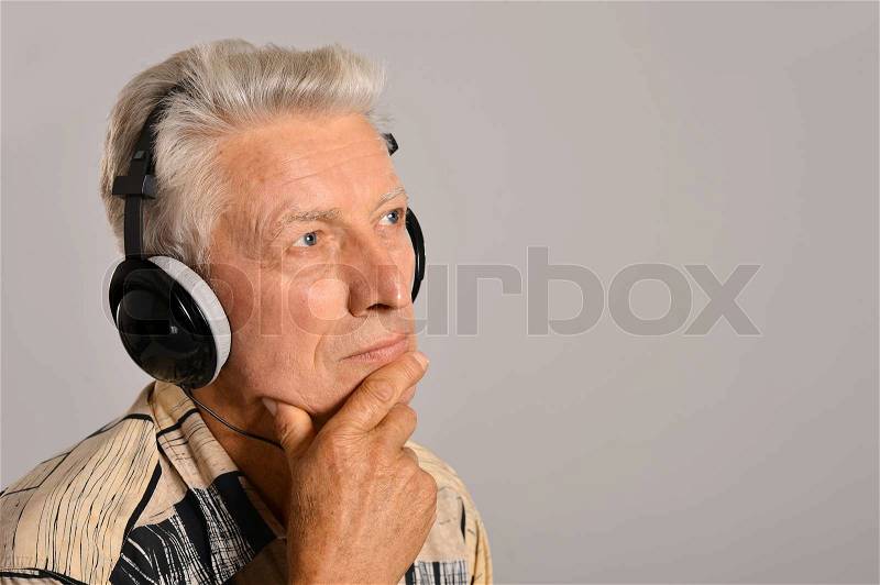 Senior man listen music in headphones on a gray background, stock photo