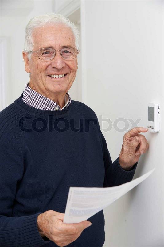 Smiling Senior Man With Bill Adjusting Central Heating Thermostat, stock photo