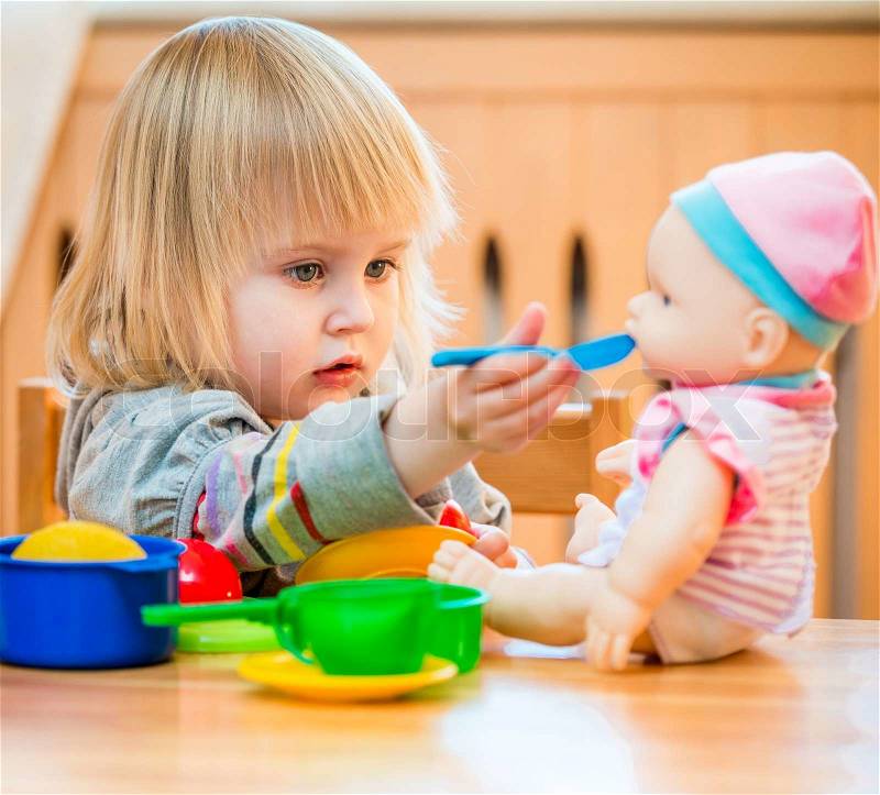 Girl feeding a doll at home in the children\'s room, stock photo