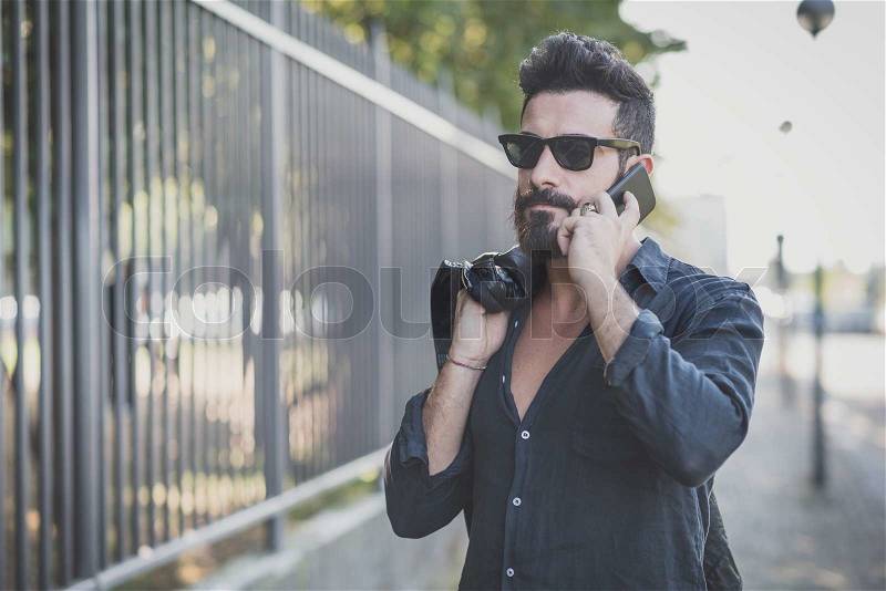 Young handsome attractive bearded model man using smartphone in urban context, stock photo