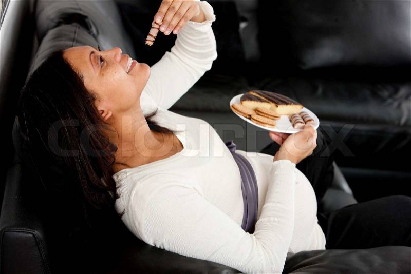 A pregnant woman on a sofa eating junk food, stock photo