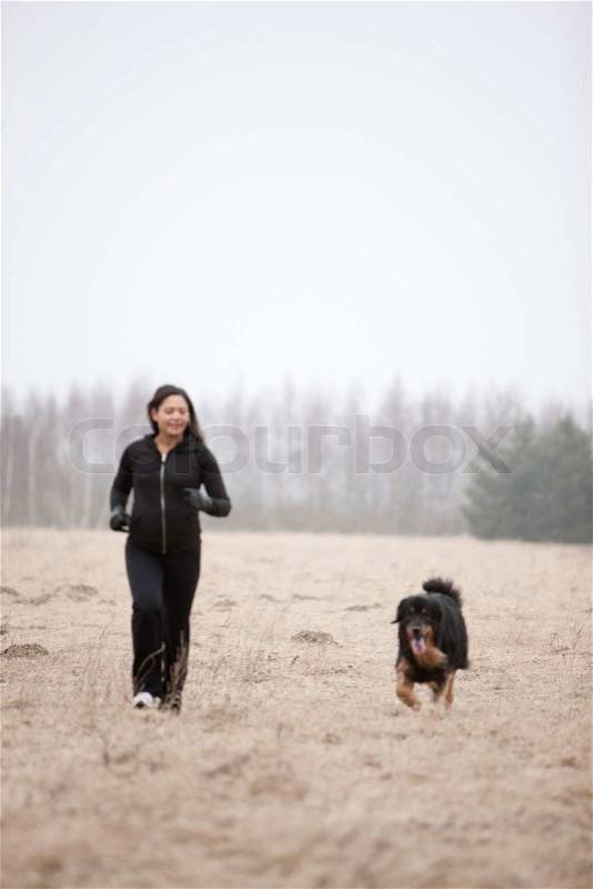 A pregnant woman and her pet dog running in the field, stock photo