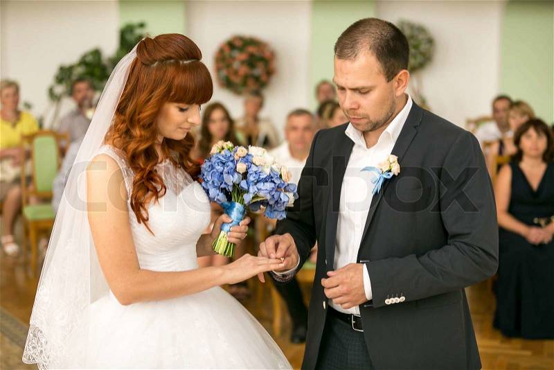 Portrait of handsome groom putting wedding ring on brides hand at registry office, stock photo