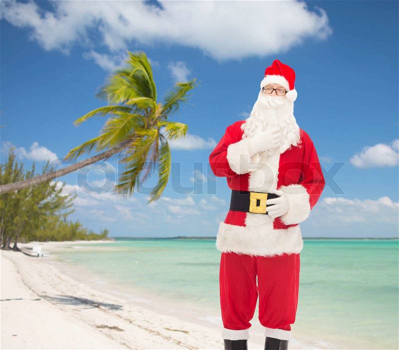 Christmas, holidays and people concept - man in costume of santa claus over tropical beach background, stock photo