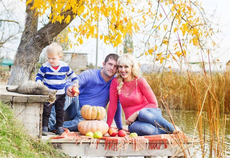Young pretty happy family son,mother and father with pumpkins near lake with cat, autumn time, stock photo