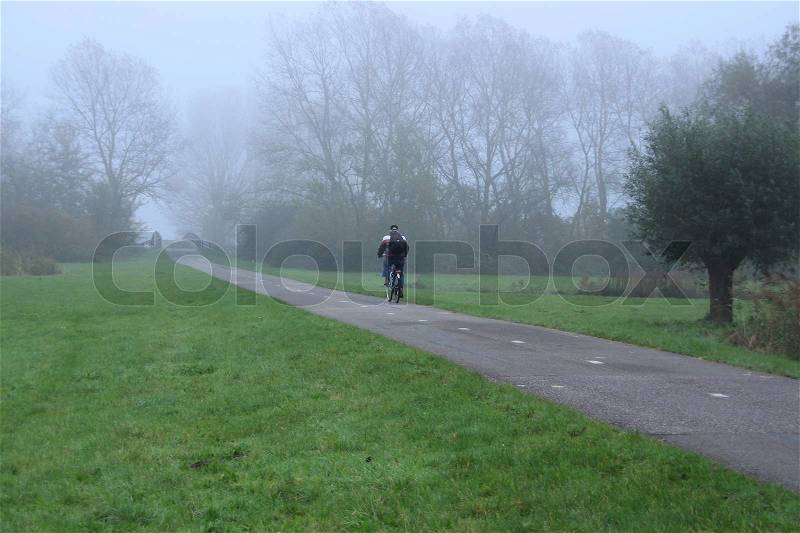 Man goes to his work on bike in fog in autumn, stock photo