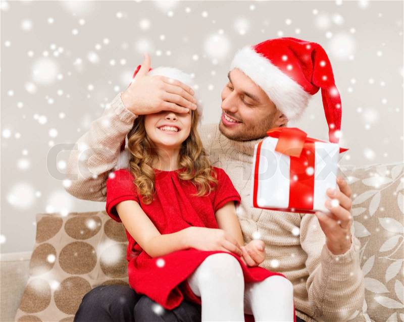 Christmas, holidays, family and people concept - smiling father and daughter in santa hats holding gift box and covering eyes at home, stock photo