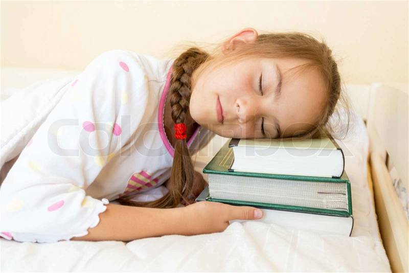 Closeup photo of little girl sleeping in bed on pile of books, stock photo