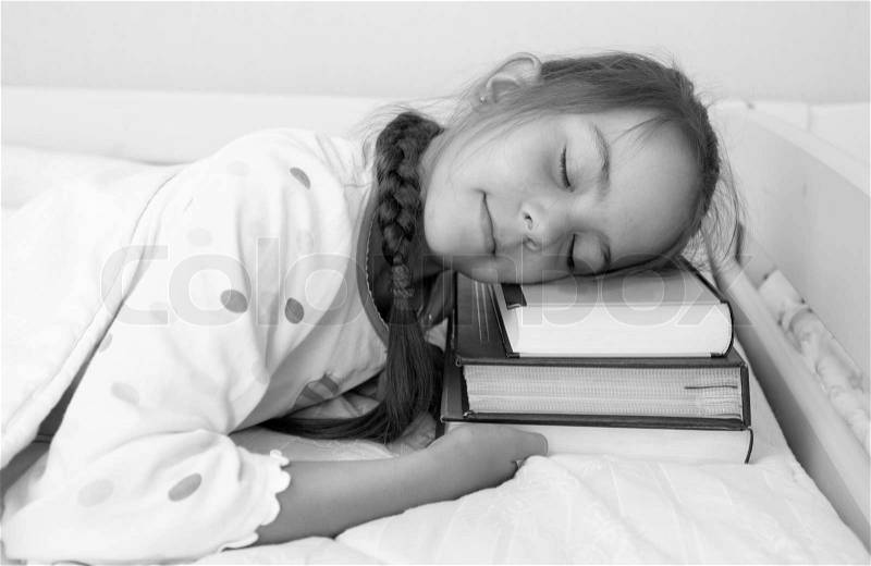 Black and white portrait of little girl sleeping on pile of books at bed, stock photo