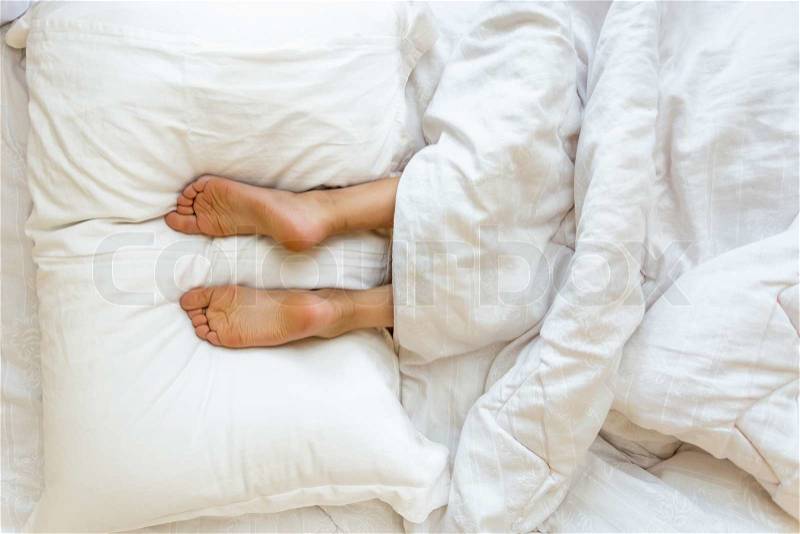 Closeup view of feet lying on soft white pillow at bed, stock photo