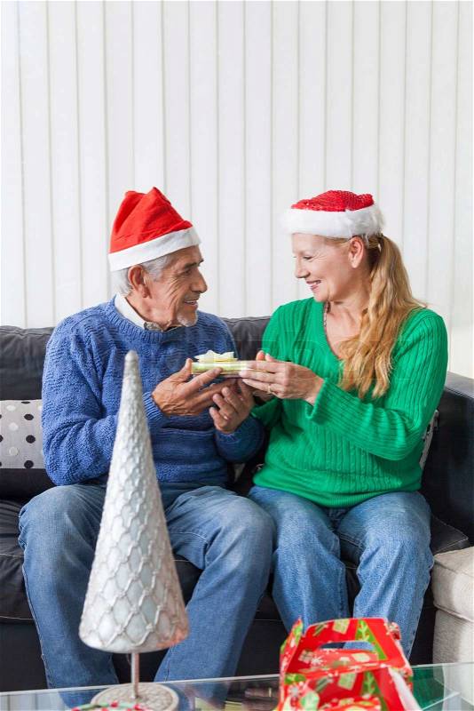 Senior couple give gift box christmas present, sitting on sofa smile, stock photo
