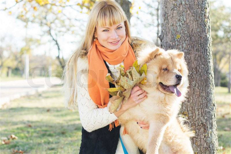 Attractive blonde smiling girl in warm clothes with her dog chauchau posing outdoors, stock photo