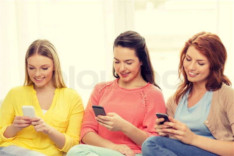 Friendship, technology and internet concept - three smiling teenage girls with smartphones at home, stock photo
