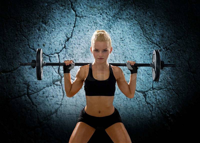Fitness, sport, powerlifting and people concept - sporty woman exercising with barbell over concrete wall background, stock photo