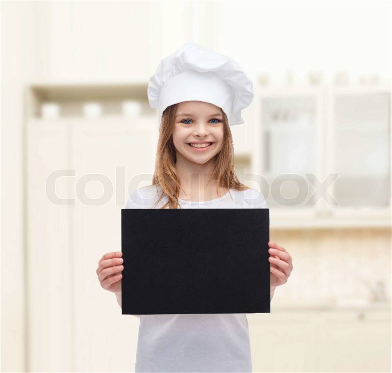 Cooking, childhood, advertisement and people concept - smiling little chef girl, cook or baker with blank black paper over kitchen background, stock photo