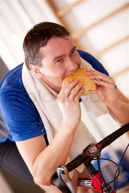 Male caucasian athlete on a bicycle while eating hamburger, stock photo