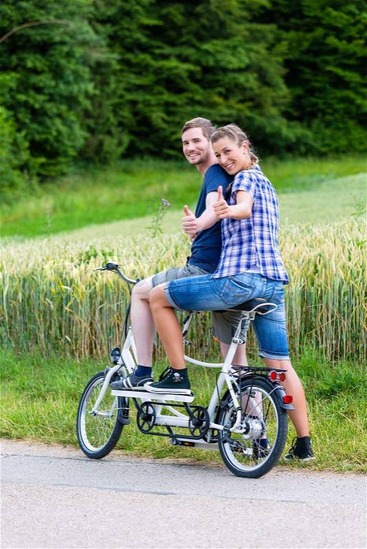 Man and woman, a couple, riding together tandem bike on country lane, stock photo