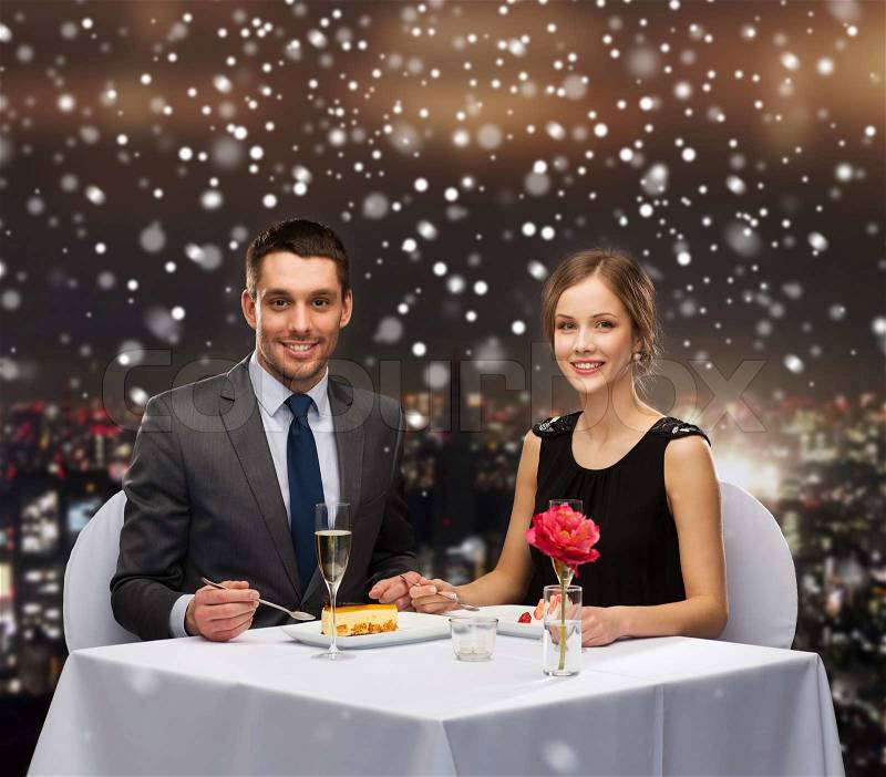 Food, christmas, holidays and people concept - smiling couple eating dessert at restaurant over snowy night city background, stock photo