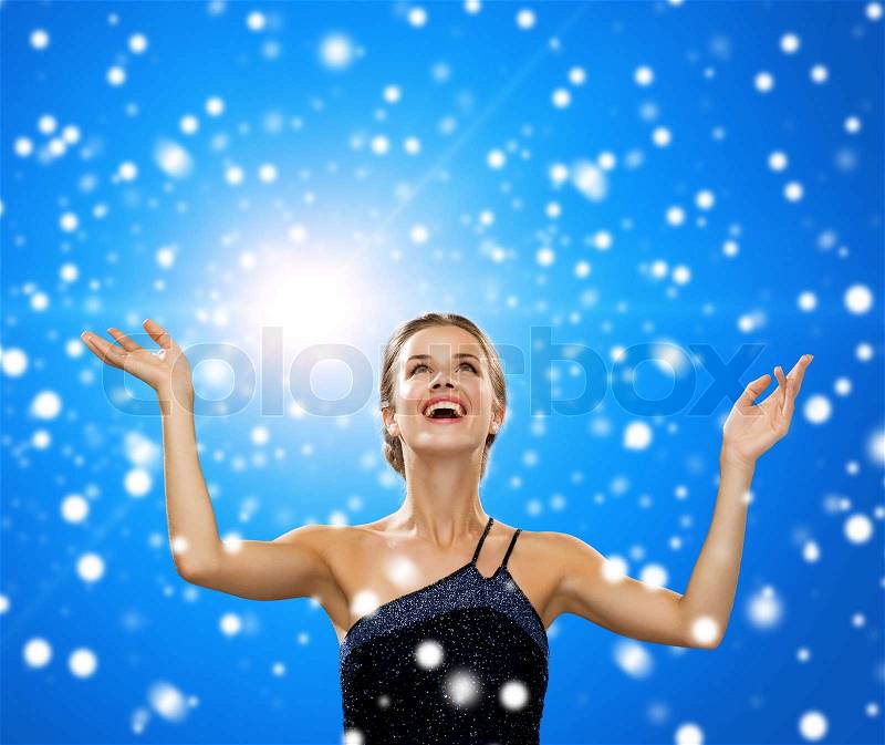 People, happiness, holidays and christmas concept - smiling woman raising hands and looking up over blue snowy background, stock photo