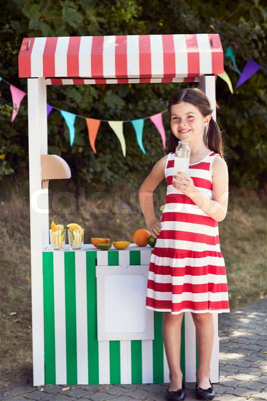 Young girl holding fruit juice bottle at fruit stall, stock photo