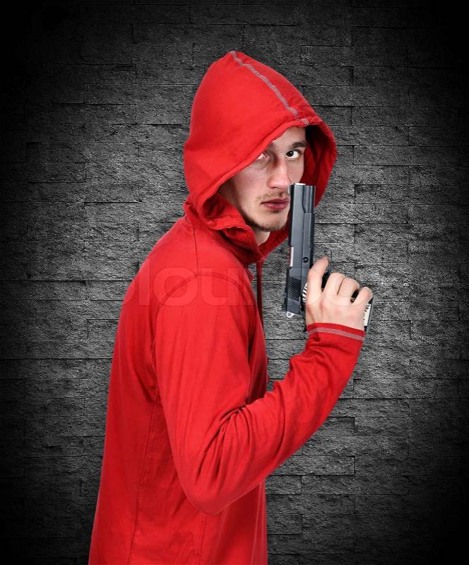 Young robber with gun on a gray background, stock photo