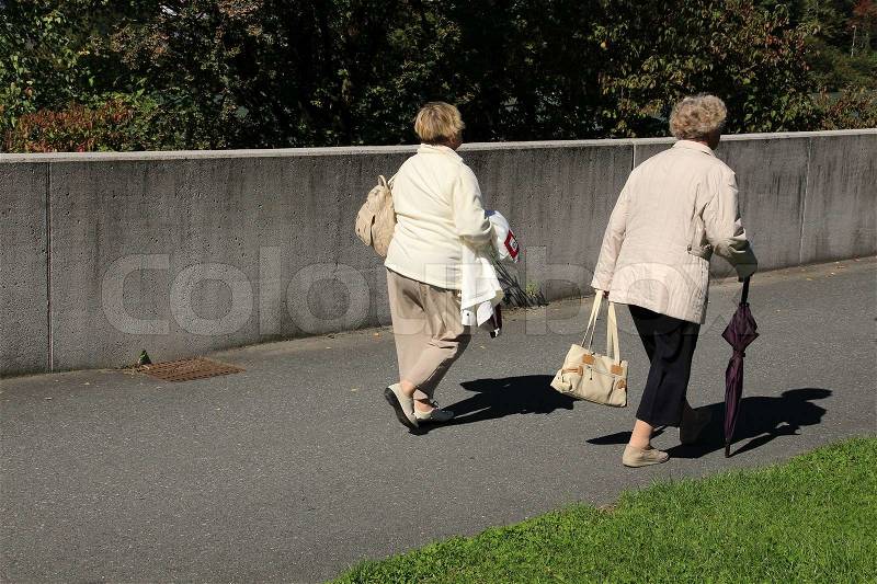 Two old ladies, family, walking with bags along the wall in summertime in Austria, stock photo