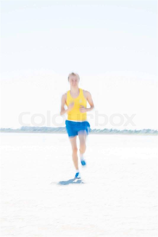 Young male runner running on a empty beach at dawn. Blur effect, stock photo