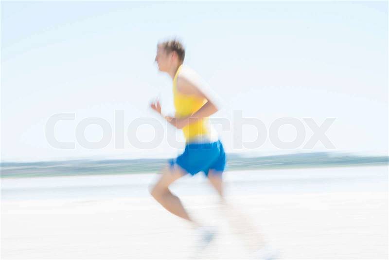 Young male runner running on a empty beach at dawn. Blur effect, stock photo