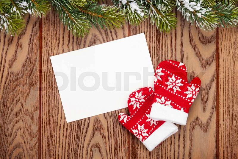 Christmas greeting card or photo frame and mittens over wooden table with snow fir tree. View from above, stock photo