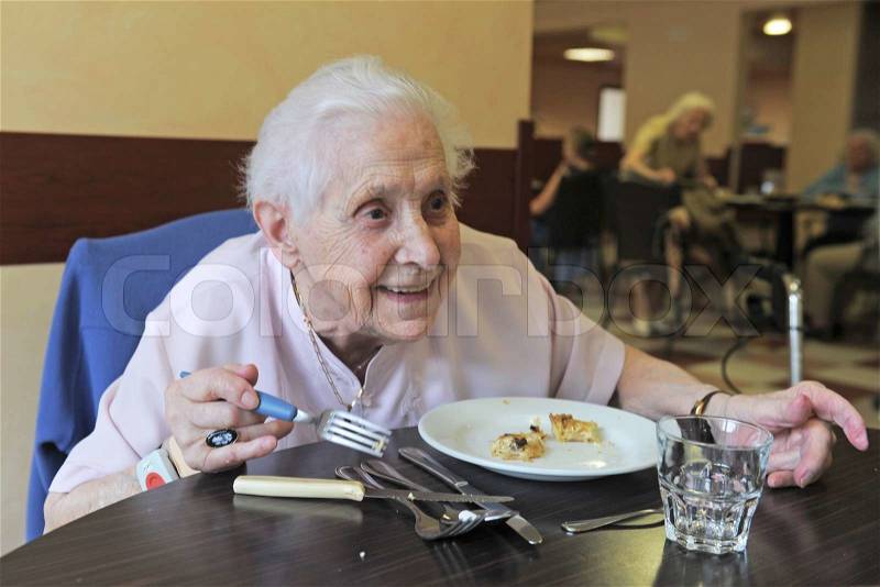 Senior woman smiling and eating in a retirement facility, stock photo